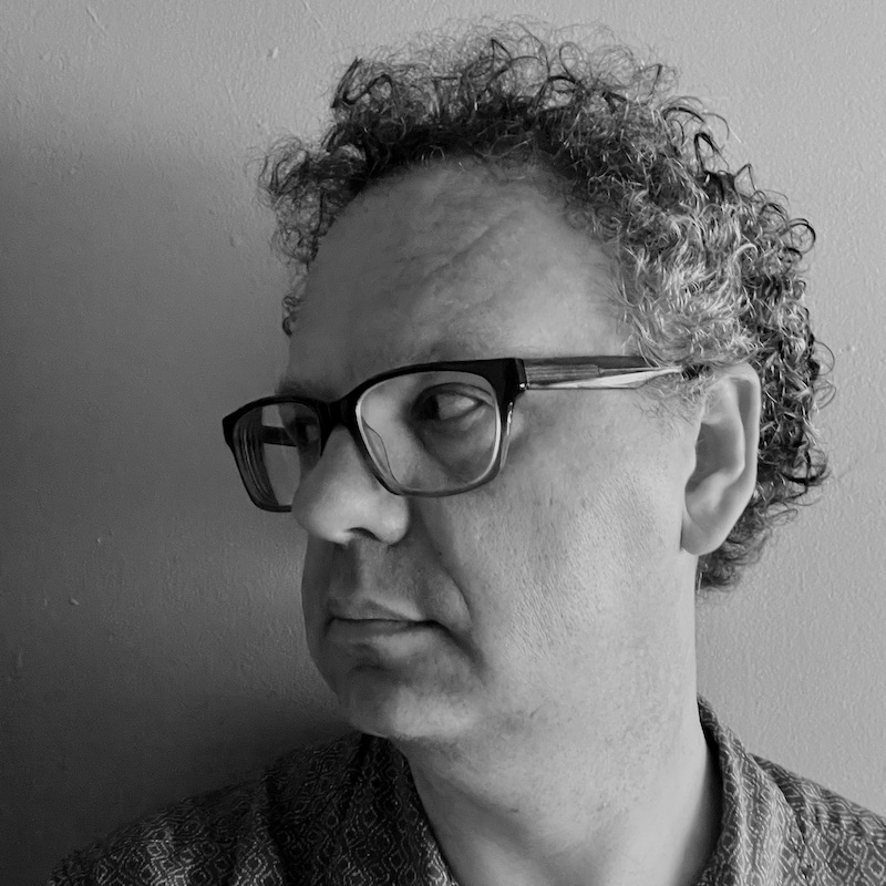 Black & White selfie of Matthew, taken indoors. He's a white man with glasses and graying but dark curly hair.